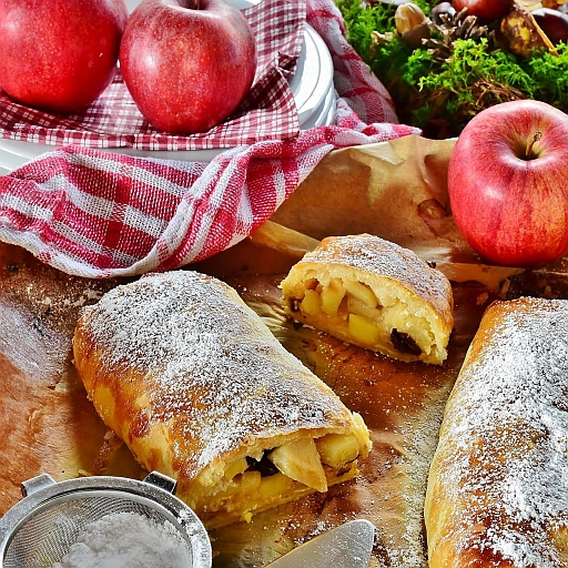 A roll of apple strudel on a counter with fresh apples